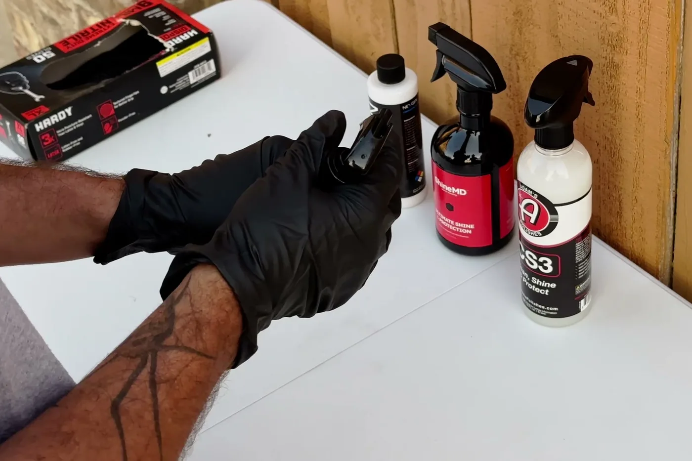 Gloved hand gliding a red clay mitt across a wet dark bonnet, the panel flooded with lubricant