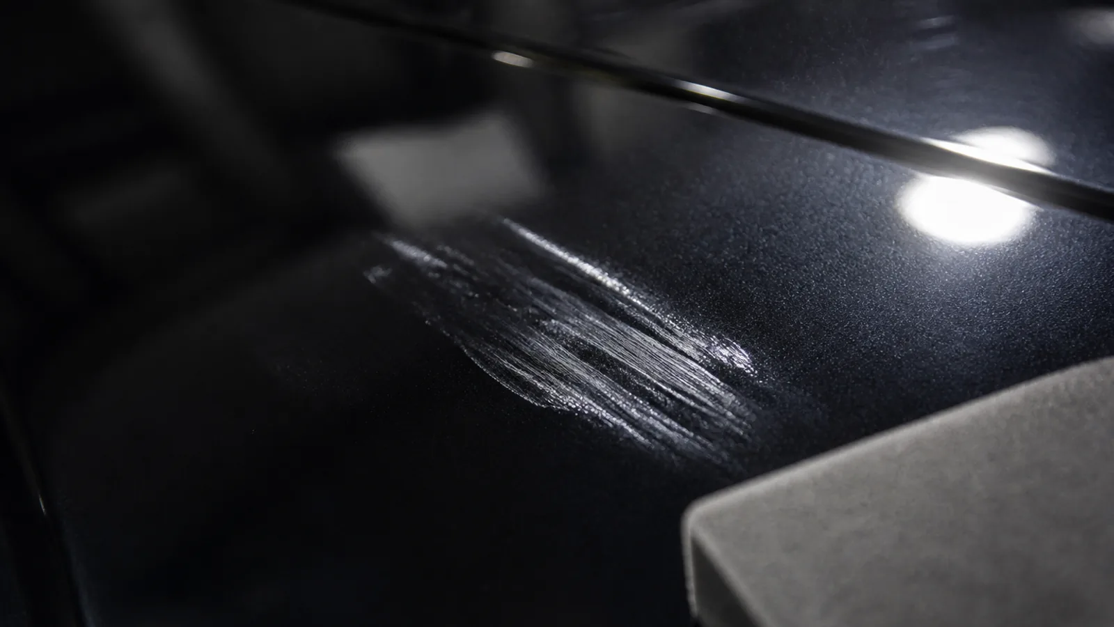 Dark car panel under inspection light showing a cloudy streaky high spot of poorly levelled ceramic coating