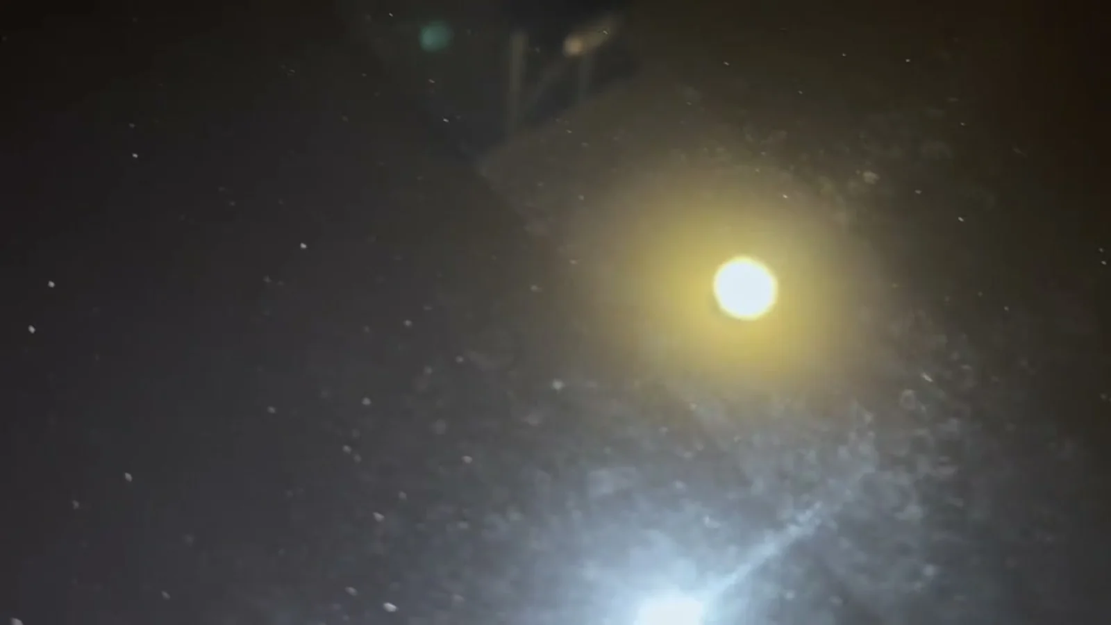 Dark coated bonnet at night under a raking flashlight beam, fine dust particles picked out across the surface