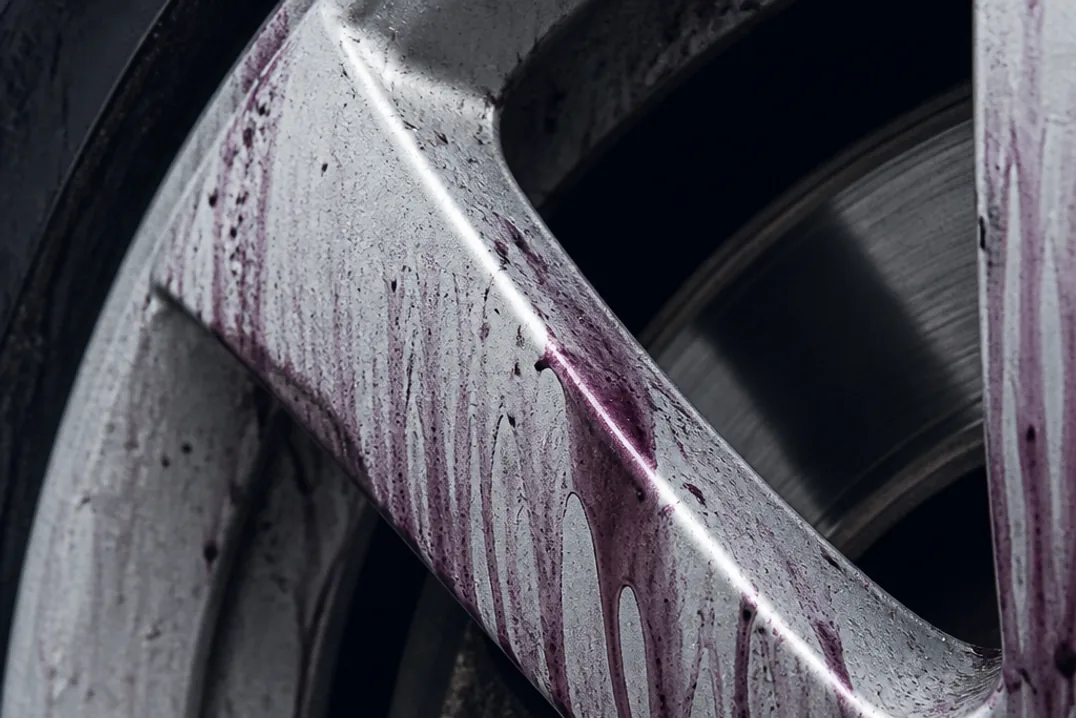Macro of iron remover reacting on an alloy wheel, purple-red streaks bleeding from embedded brake dust particles