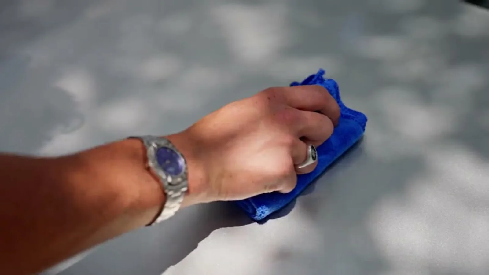 Hand pressing a folded blue microfibre towel flat against a pale panel, reflections breaking across the surface