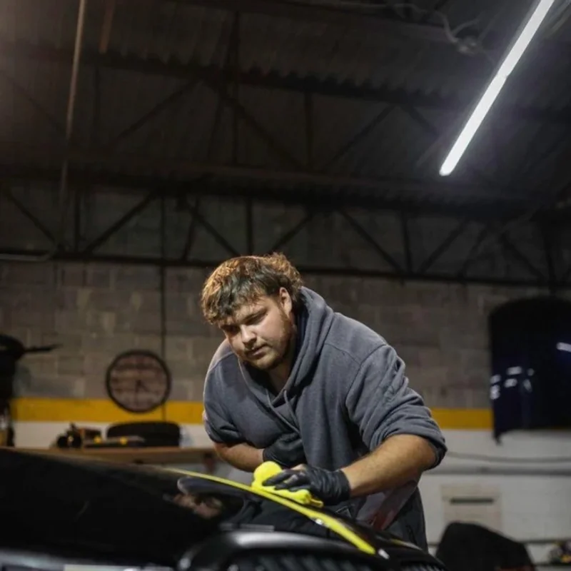 Ducky applying coating with a yellow foam applicator on a black BMW in the shop