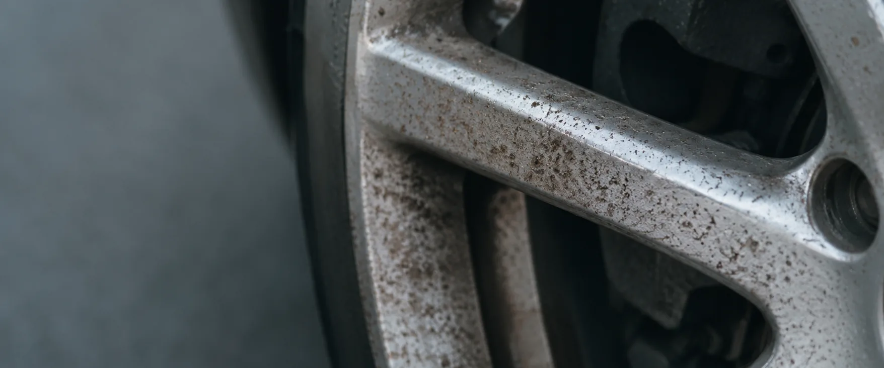 Close view of a silver alloy wheel with a heavy layer of sintered brake dust across the spokes and barrel